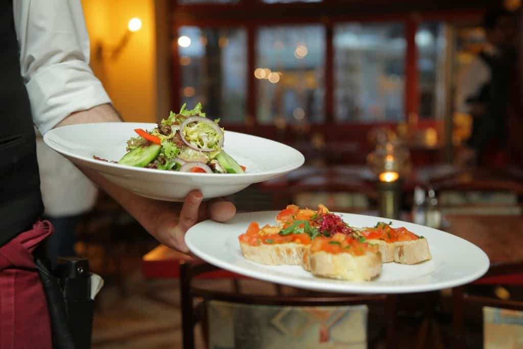 Two plates of food being served at a restaurant, a salad and bruschetta dish
