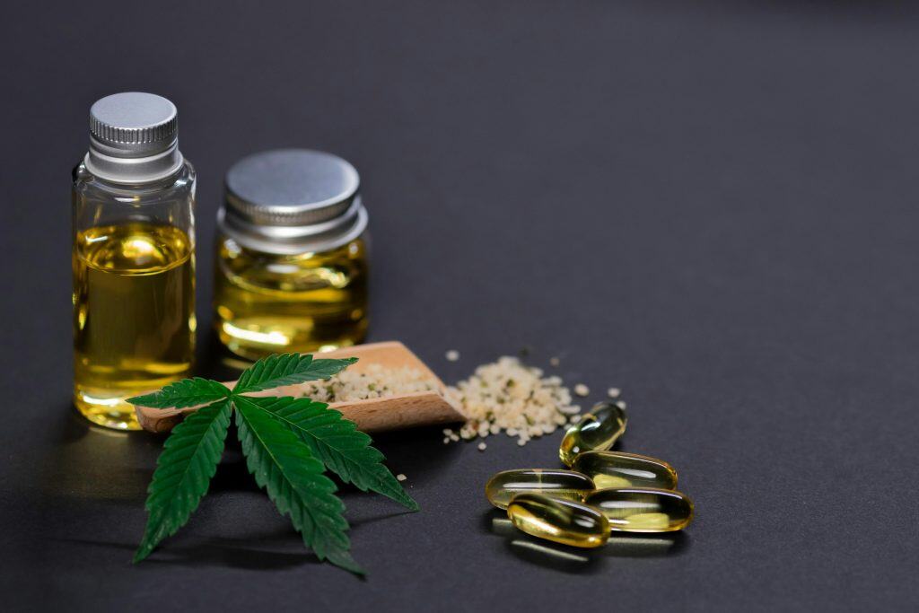A cannabis leaf pictured with related products, like CBD capsules and concentrate