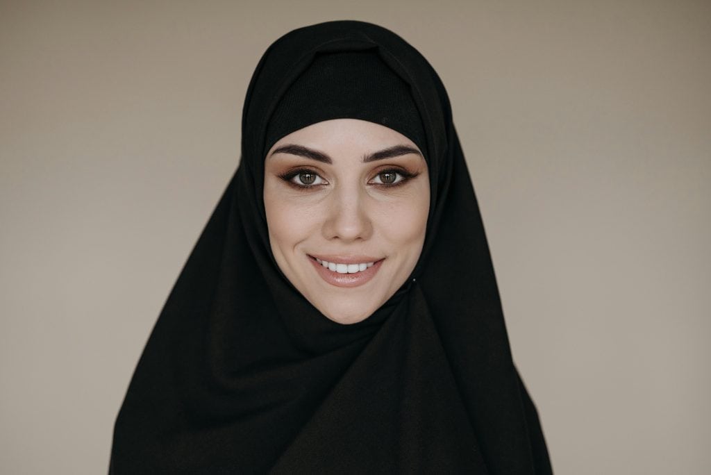 A Muslim woman wearing a black hijab, facing the camera smiling, representing What is the Hijab and is it Required in Islam?