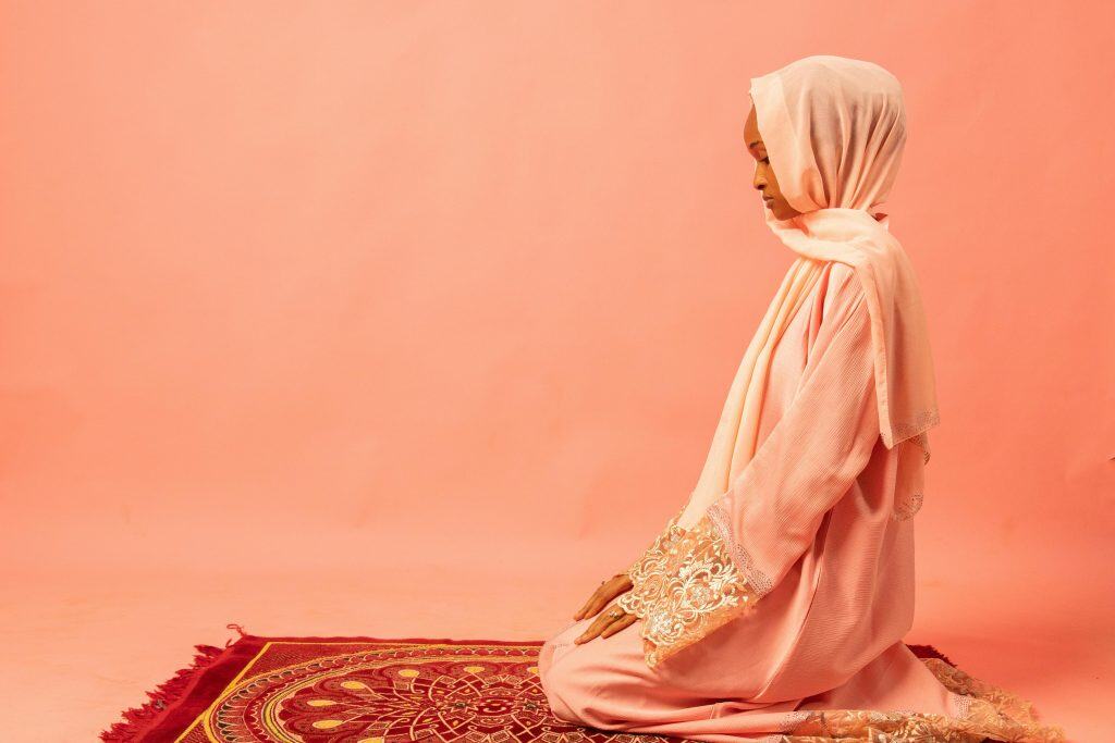A Muslim woman wearing a pink hijab kneeling in prayer, representing menses in Islam