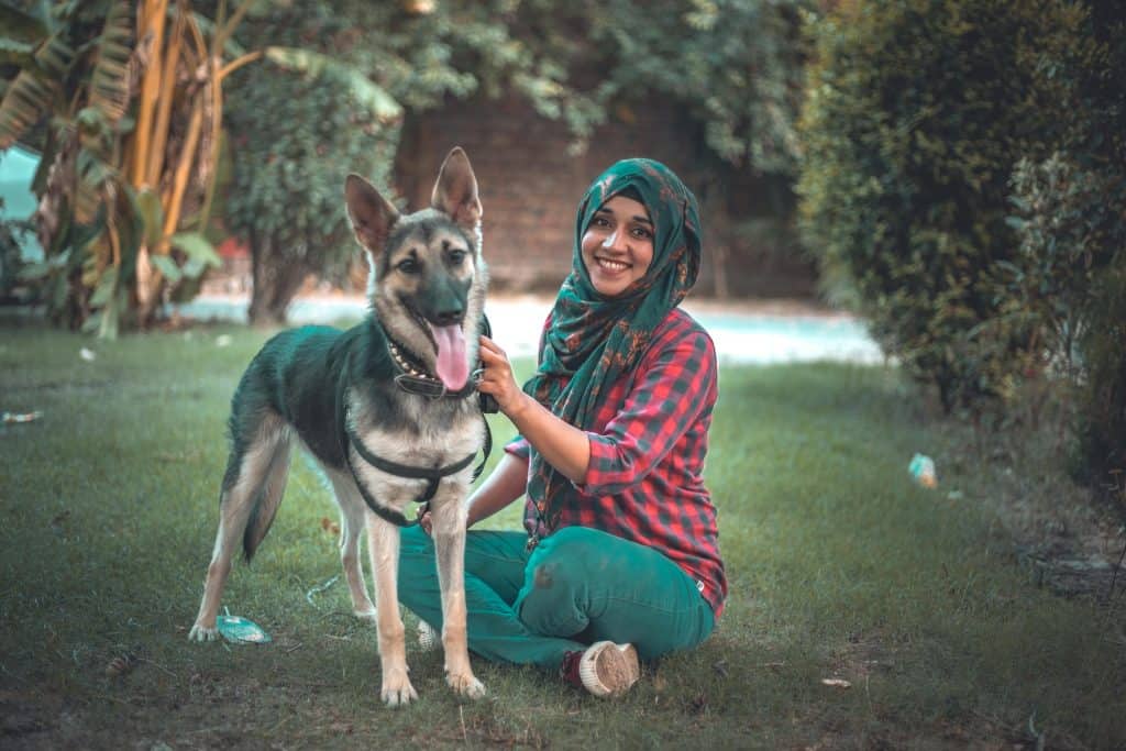 A Muslim woman wearing hijab sitting next to her pet dog in a park, representing Can Dogs Be Kept as Pets in Islam?